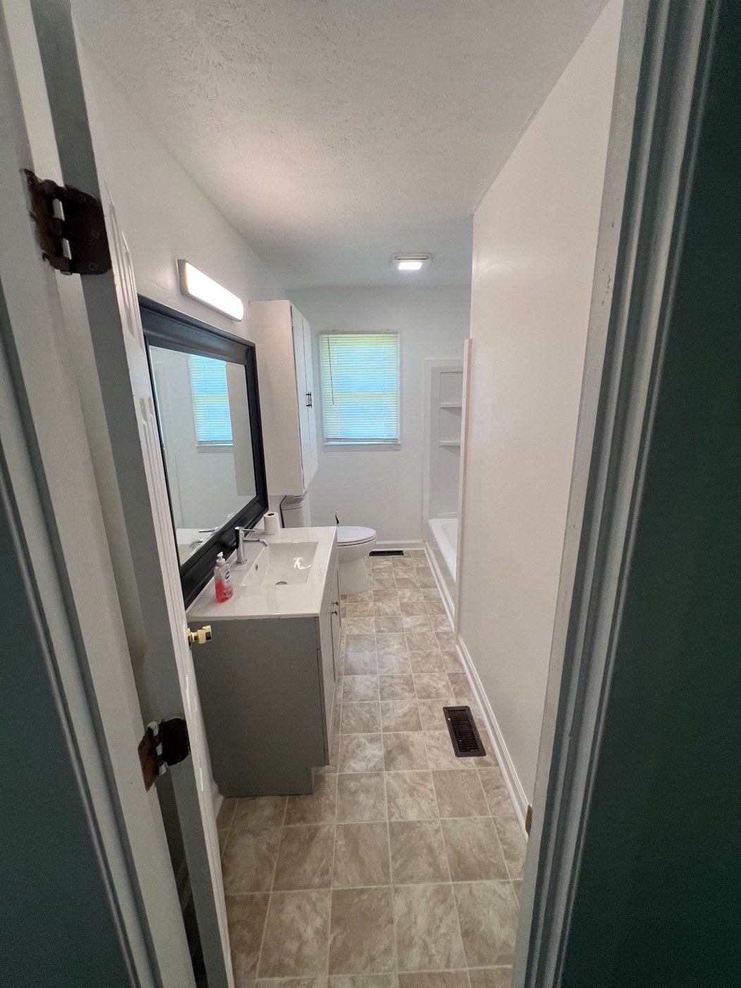 Finished bathroom viewed from the doorway, with vanity, mirror, flooring and tub surround.