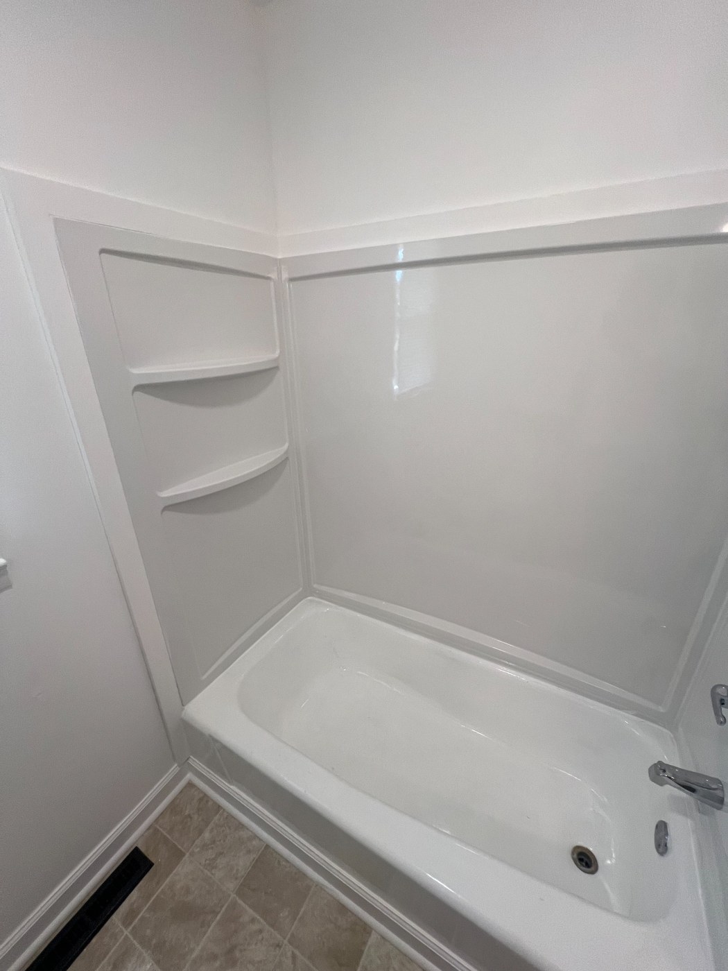 White bathtub and shower surround with corner shelves and finished trim.