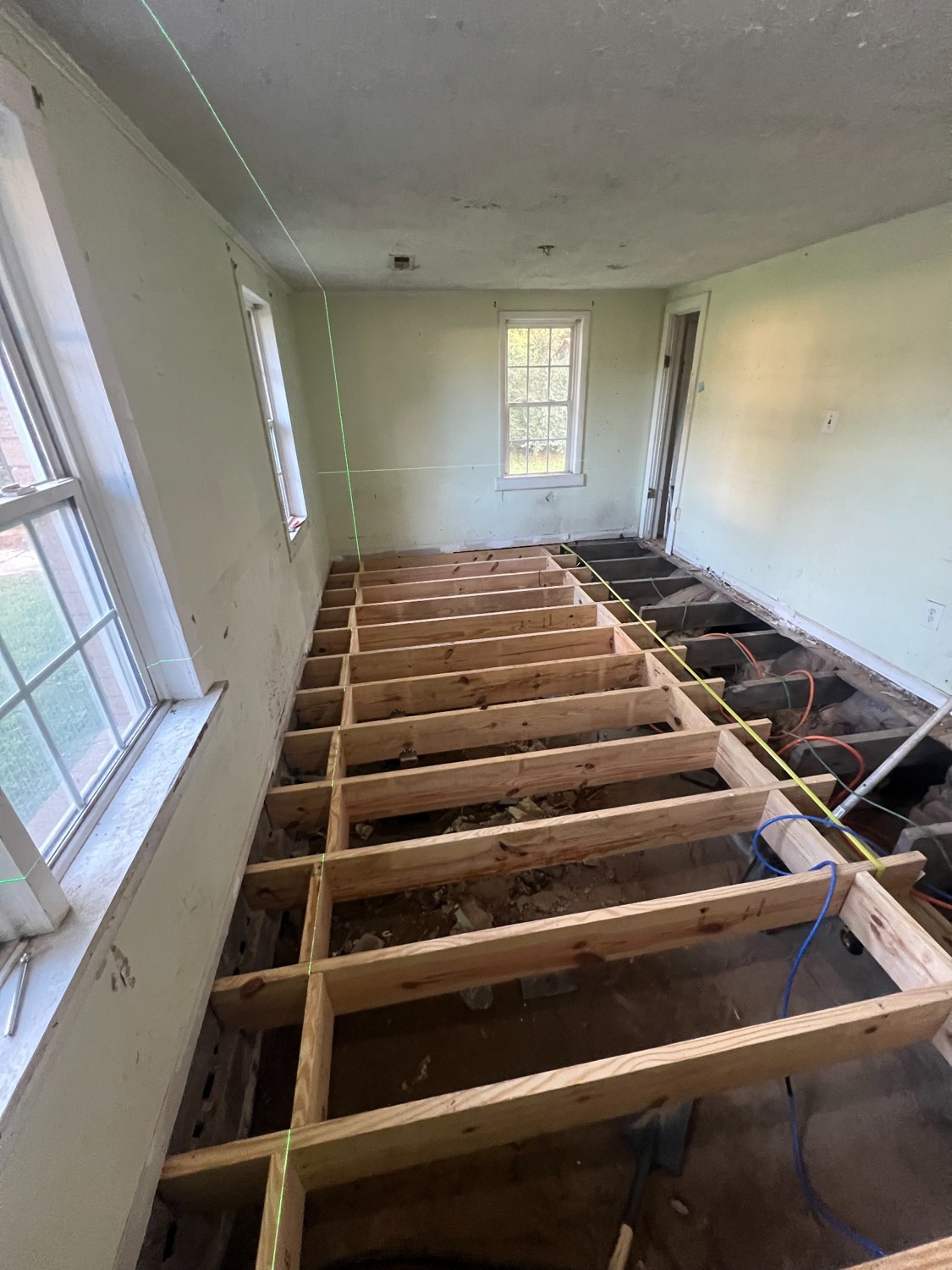 Replacement wooden floor joists installed in a room, with open framing and a green leveling laser visible.