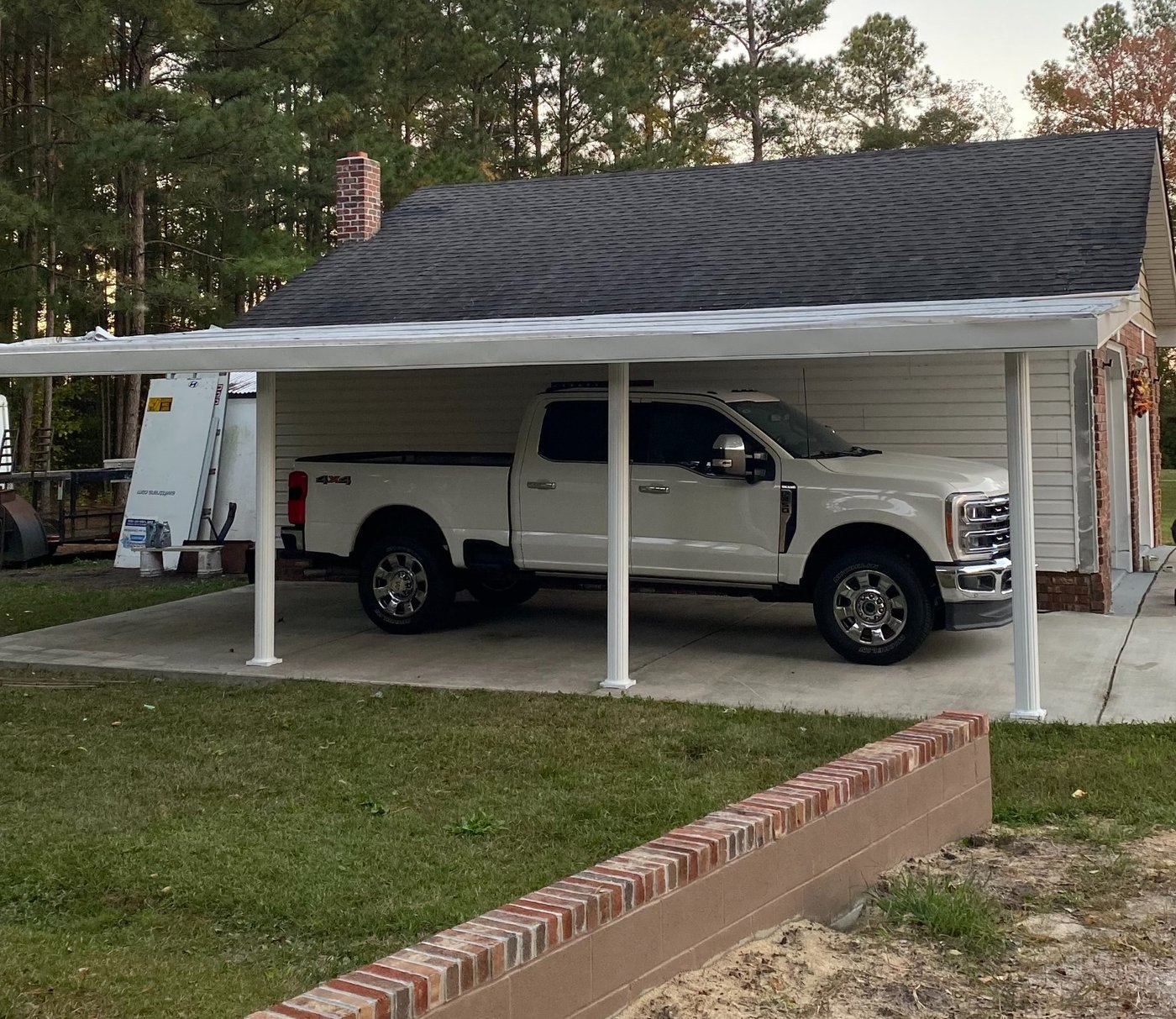 Covered parking area with white posts and siding next to a brick building.
