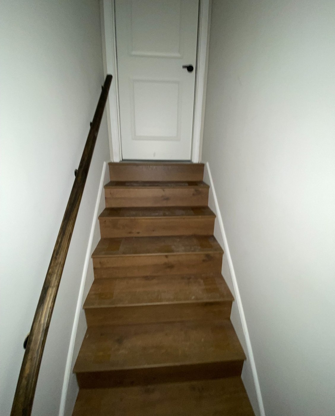 Wood-finished interior staircase with white walls and a dark handrail.
